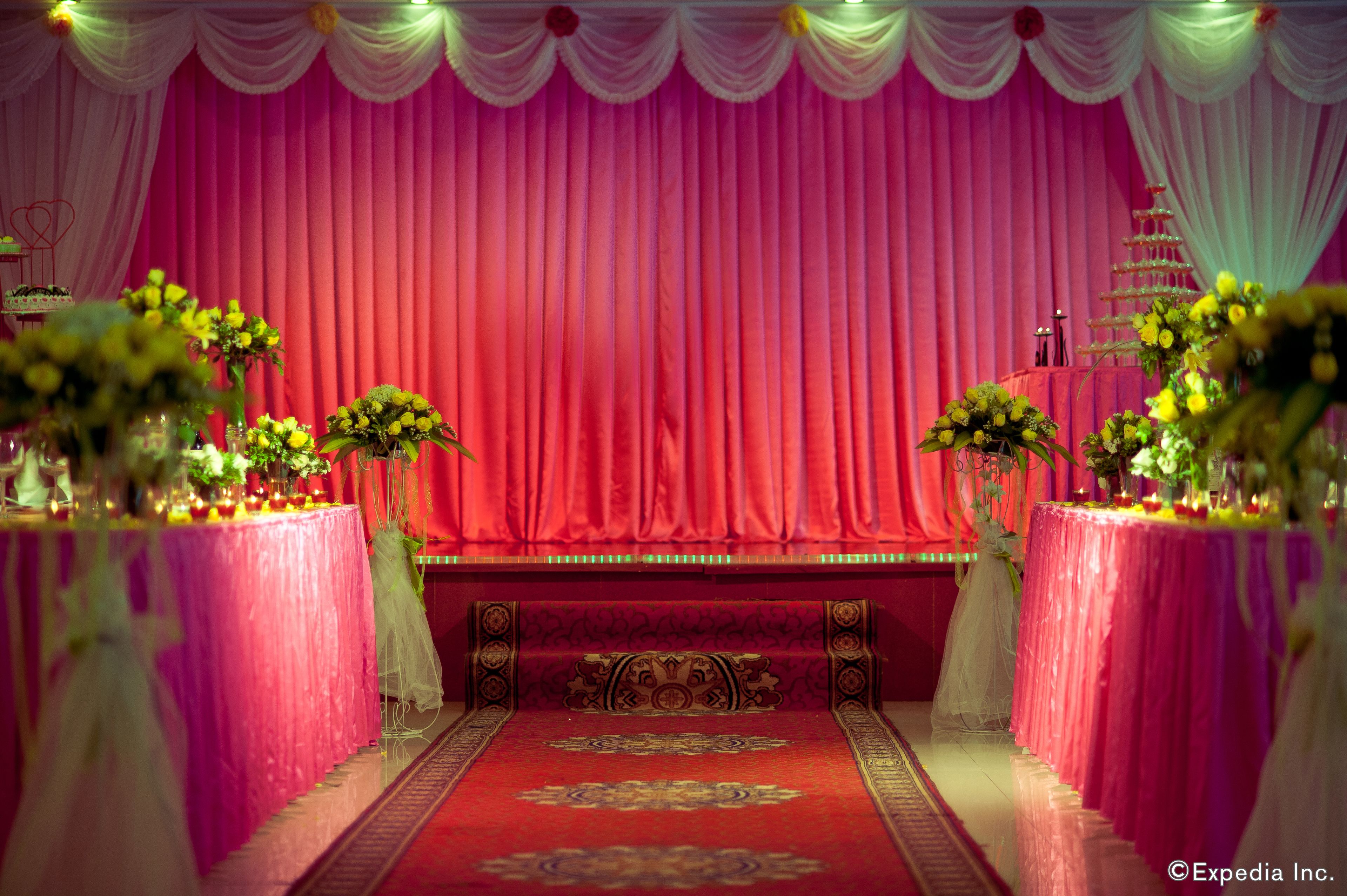 A stage with a red curtain backdrop, floral centerpieces on tables, and a decorative chair in the foreground.