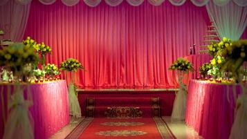 Een podium met een rode gordijnenachtergrond, bloemstukken op tafels en een decoratieve stoel op de voorgrond.