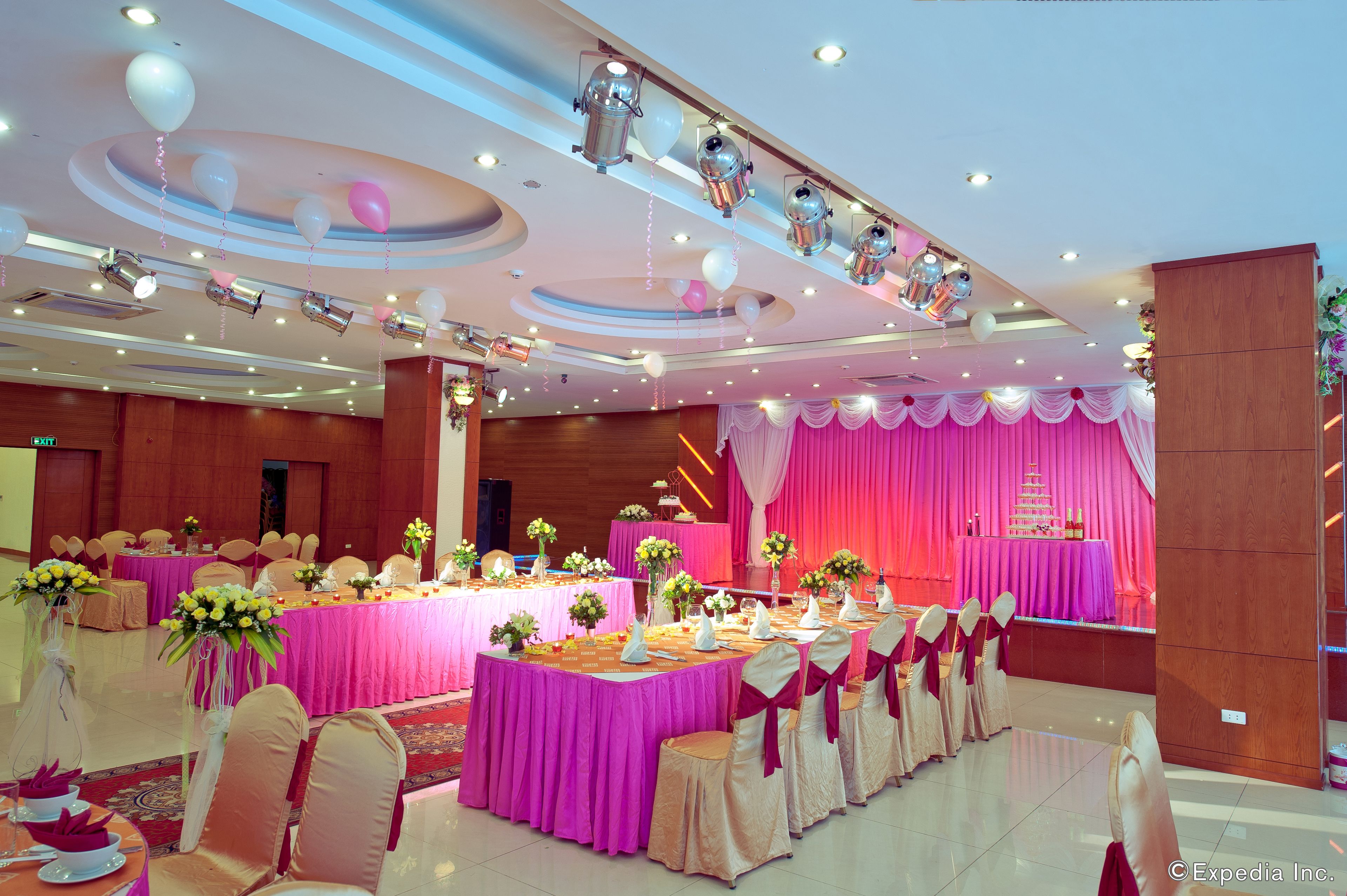 Une salle de banquet avec des tables rondes, des rideaux roses et des centres de table floraux.
