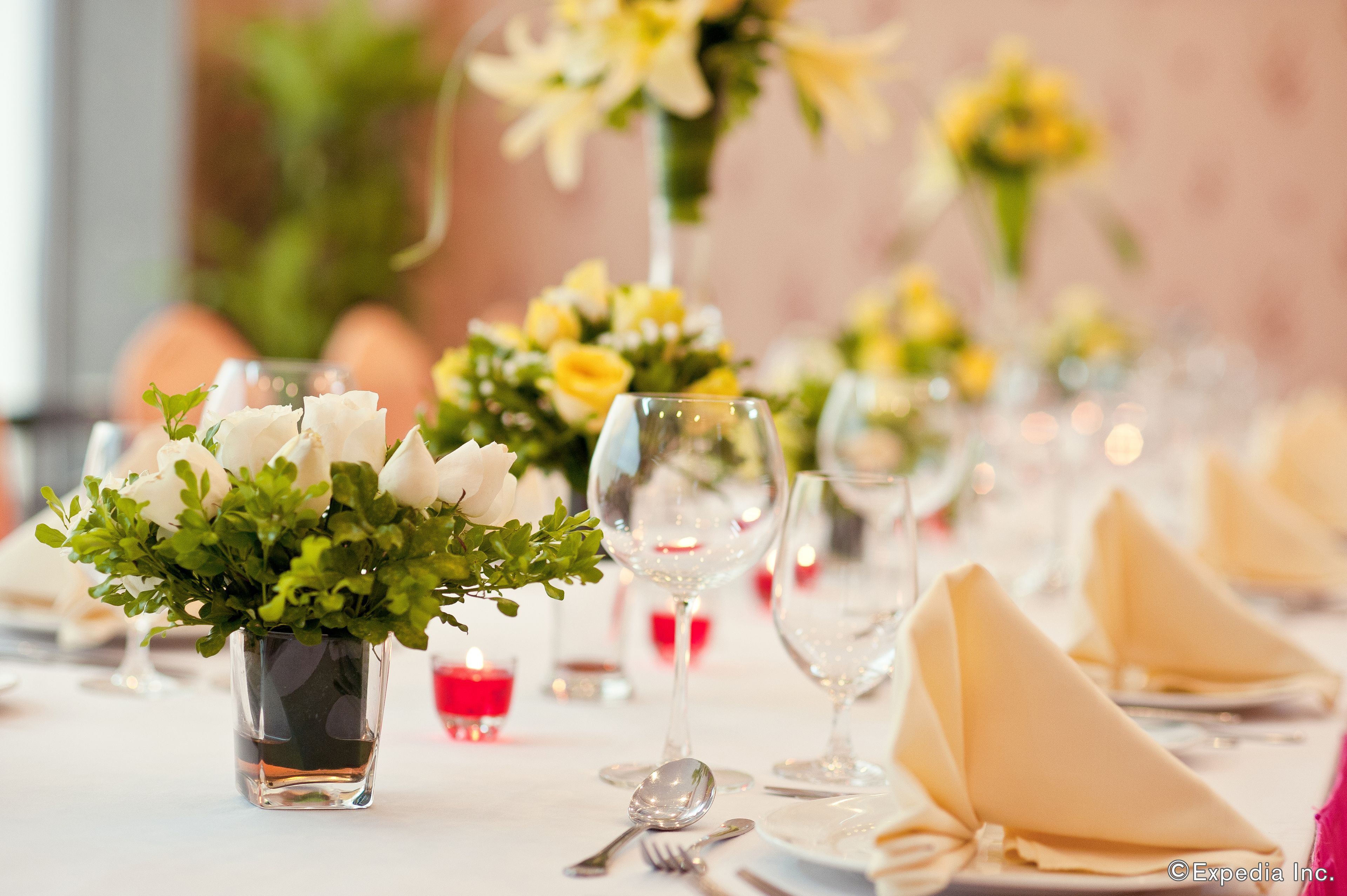 A table set with white napkins, silverware, and clear glassware, adorned with small potted plants and candles.