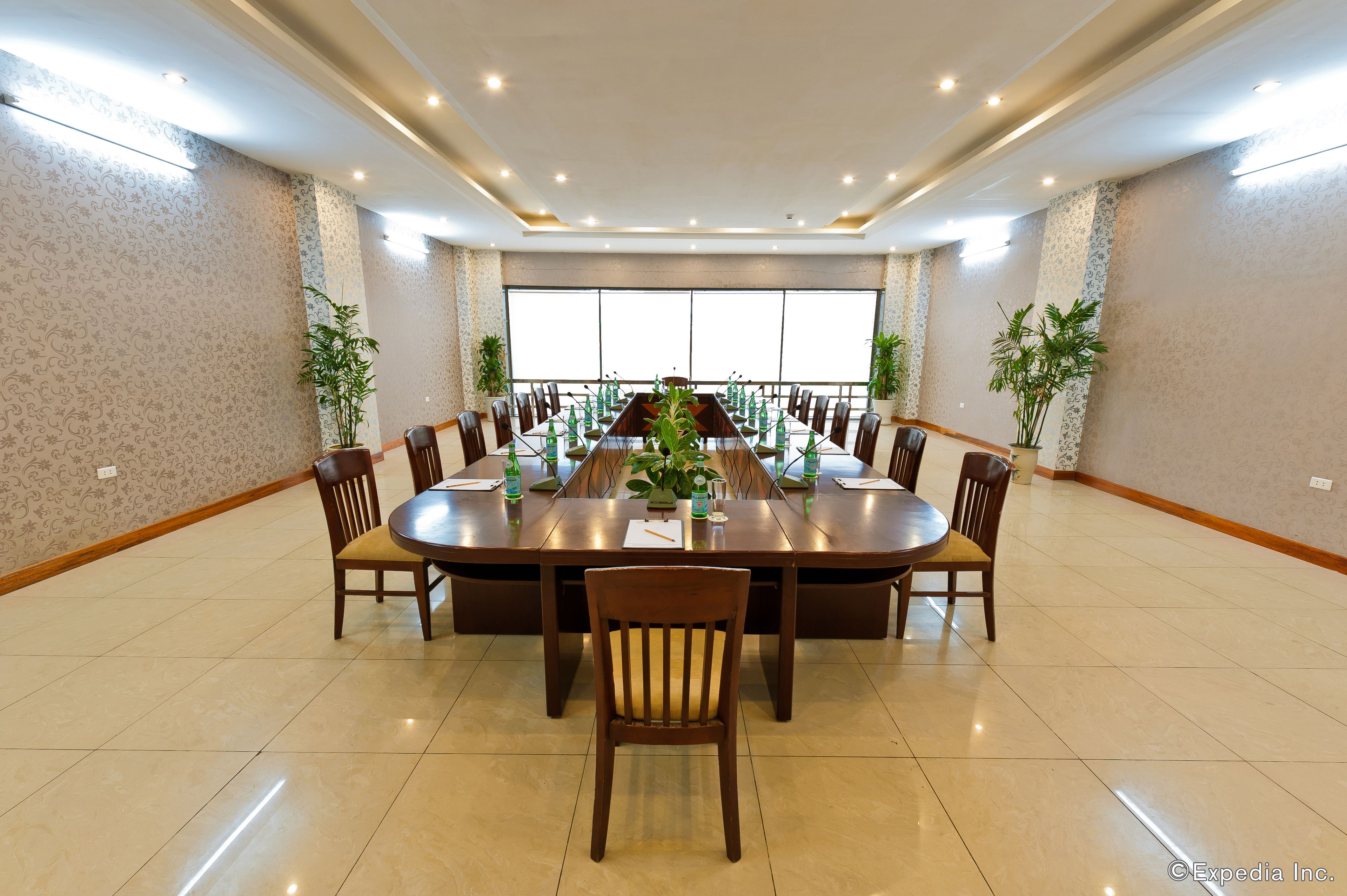 Un salón de conferencias con una larga mesa, sillas, plantas en macetas y un amplio ventanal.