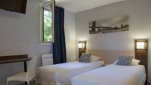Une chambre d’hôtel avec deux lits simples, un bureau, une chaise et une fenêtre donnant sur un espace verdoyant.