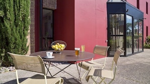 Un espace extérieur aménagé avec une table ronde et quatre chaises, un saladier rempli de citrons et deux boissons.