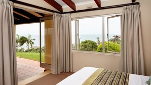 A bedroom with a large bed, a view of the ocean, and a sliding glass door leading to an outdoor area. - First Group Chaka Rock Chalets (Ballito)