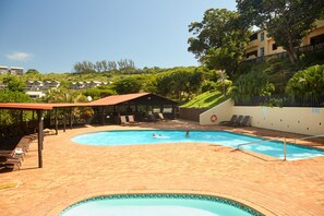 Una piscina al aire libre, sombrillas, sillones reclinables de piscina