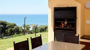 An outdoor seating area with a view of the ocean, a grill, and a table. - First Group Chaka Rock Chalets (Ballito)