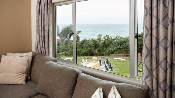 A living room with a sofa and a view of the sea through large windows. - First Group Chaka Rock Chalets (Ballito)