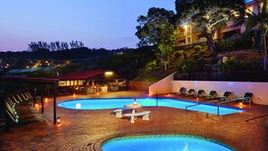 A swimming pool with a fountain, lounge chairs, and a bar area. - First Group Chaka Rock Chalets (Ballito)