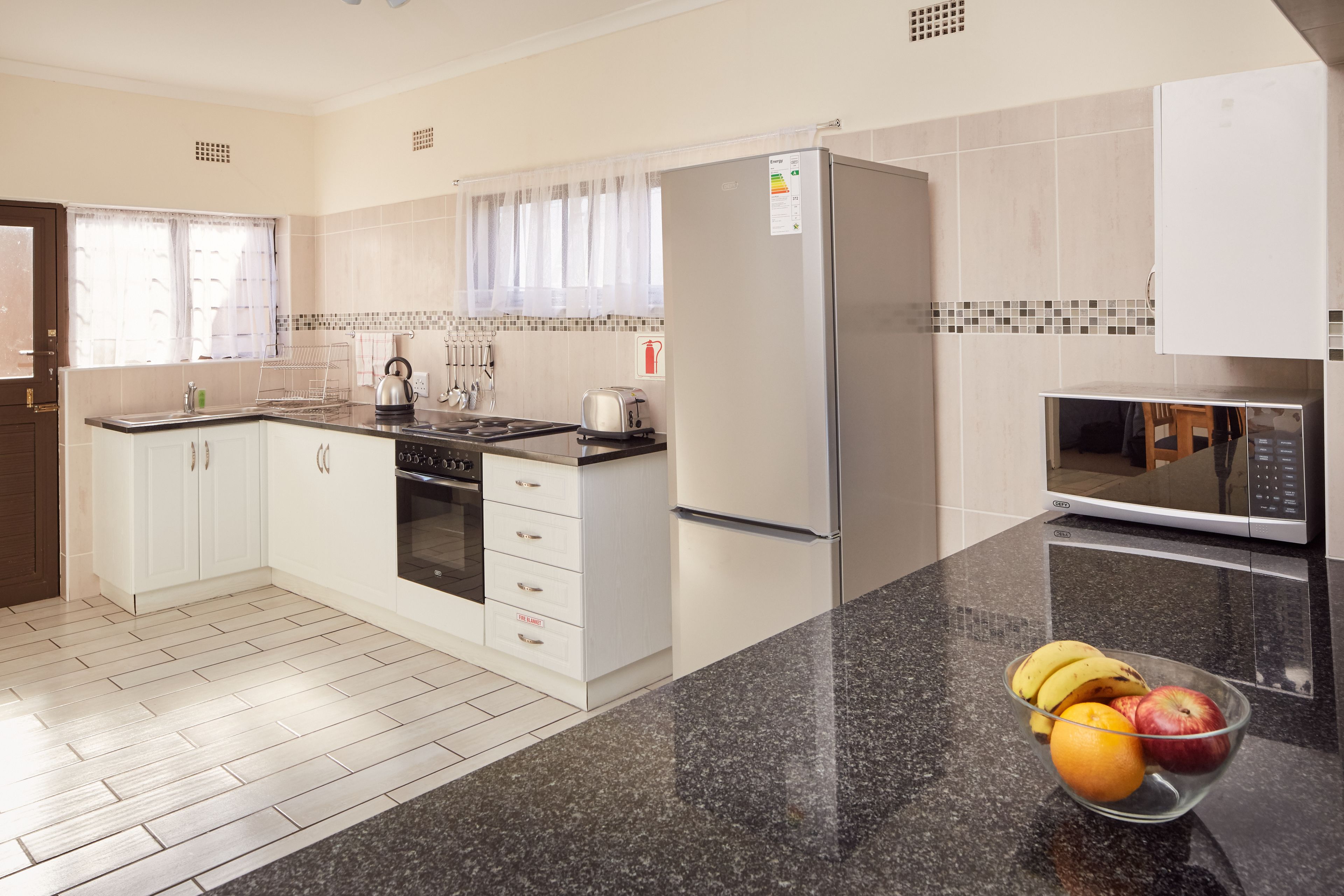 Una cocina moderna con armarios blancos, un refrigerador de acero inoxidable, un microondas y un frutero en la encimera.