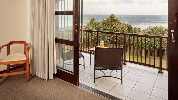 A balcony with a view of the ocean, a wooden chair, a metal chair, and a small table with a glass of orange juice. - First Group Club Hacienda (Margate)