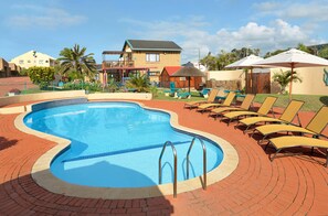 Une piscine à bords ondulés, entourée de chaises longues et d’une terrasse en briques.