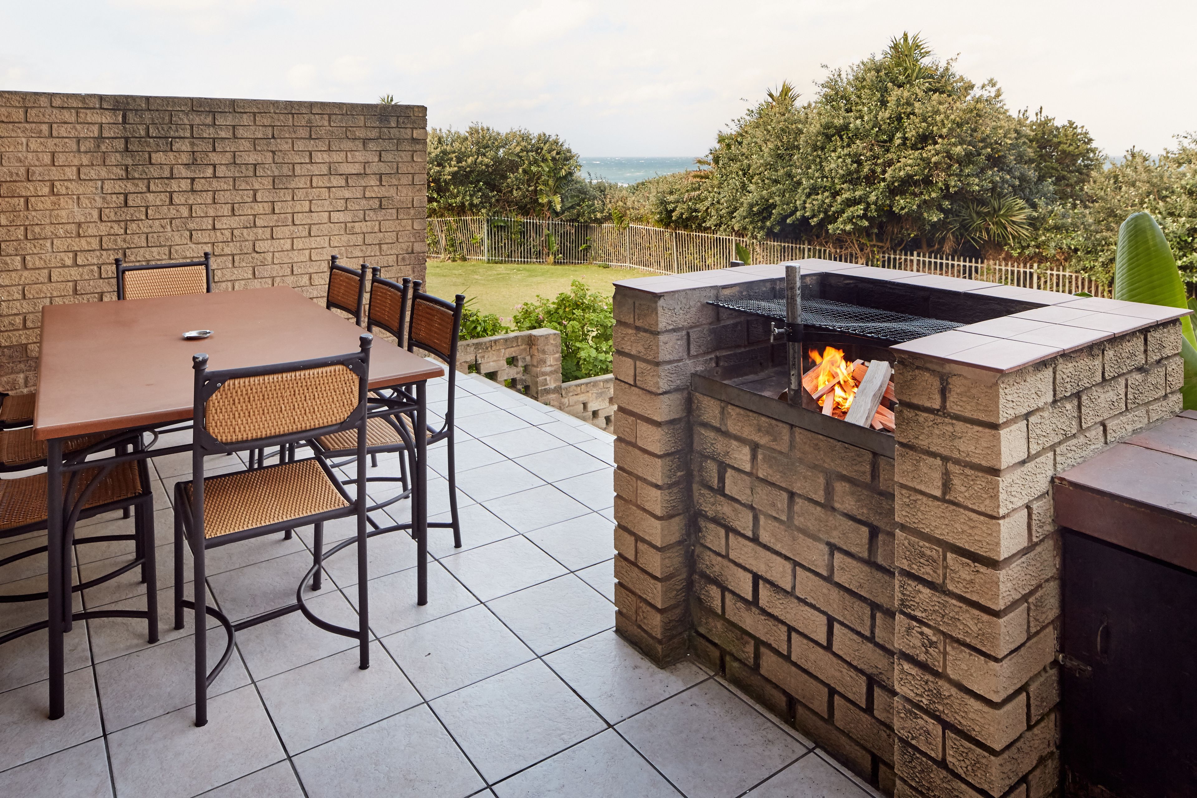 Une terrasse extérieure avec un barbecue en briques, une table à manger avec des chaises et une vue sur la mer.
