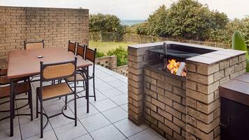 Un patio exterior con una parrilla de ladrillo, una mesa de comedor con sillas y vista al mar.