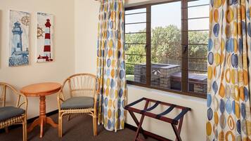 A room with a wooden table and two wicker chairs, a window with curtains, and two wall-mounted paintings.