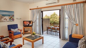 A living room with a television, blue sofas, a wooden coffee table, and a view of the outdoors through a sliding door. - First Group Club Hacienda (Margate)