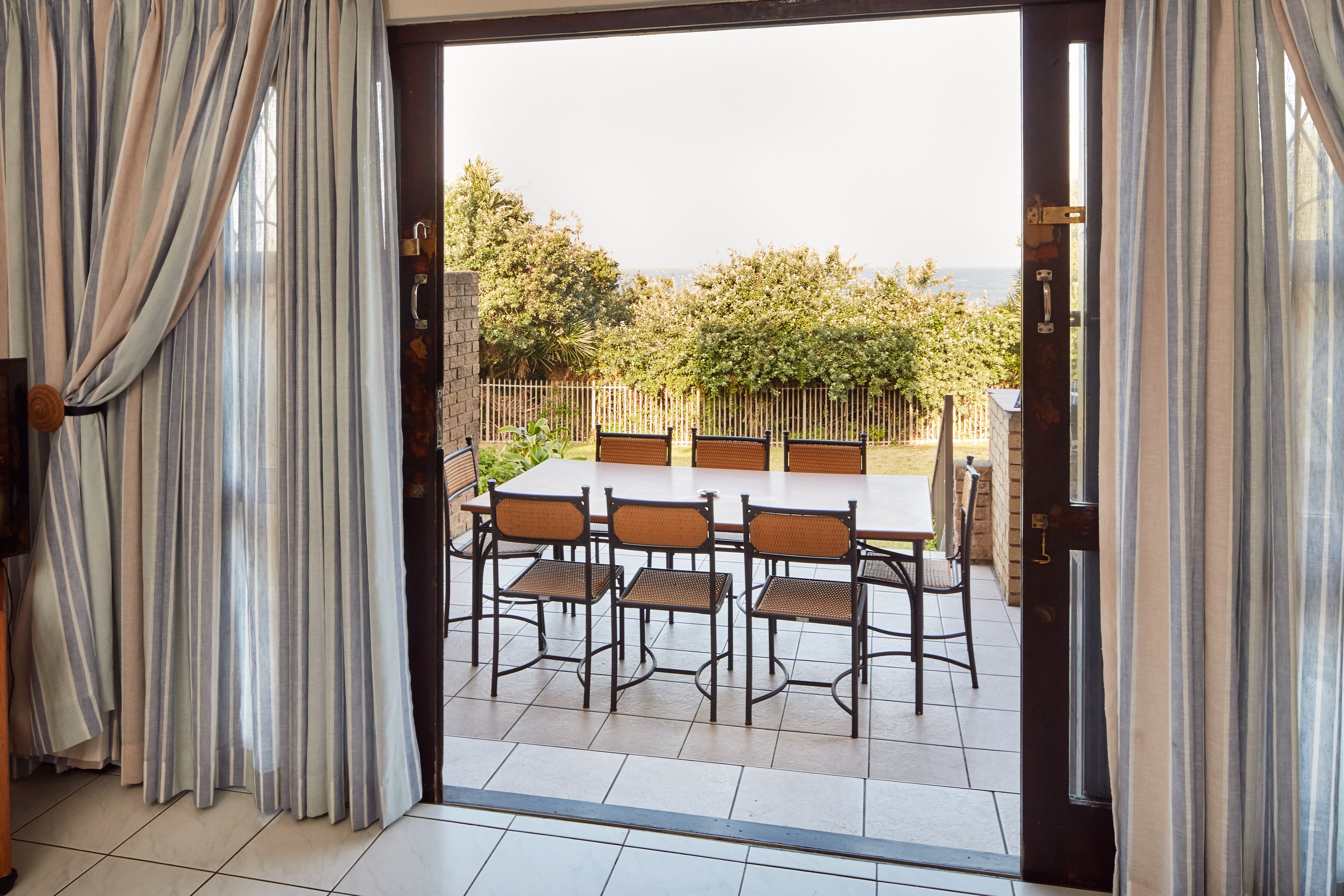 En terrasse med bord og stole, udsigt over naturen, og en dør med gardiner.