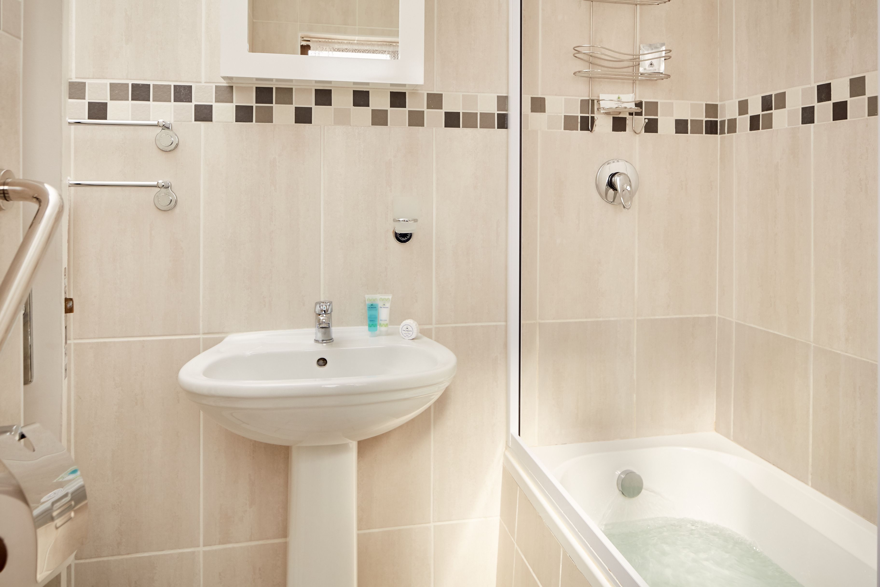 A bathroom with a sink, mirror, and bathtub.