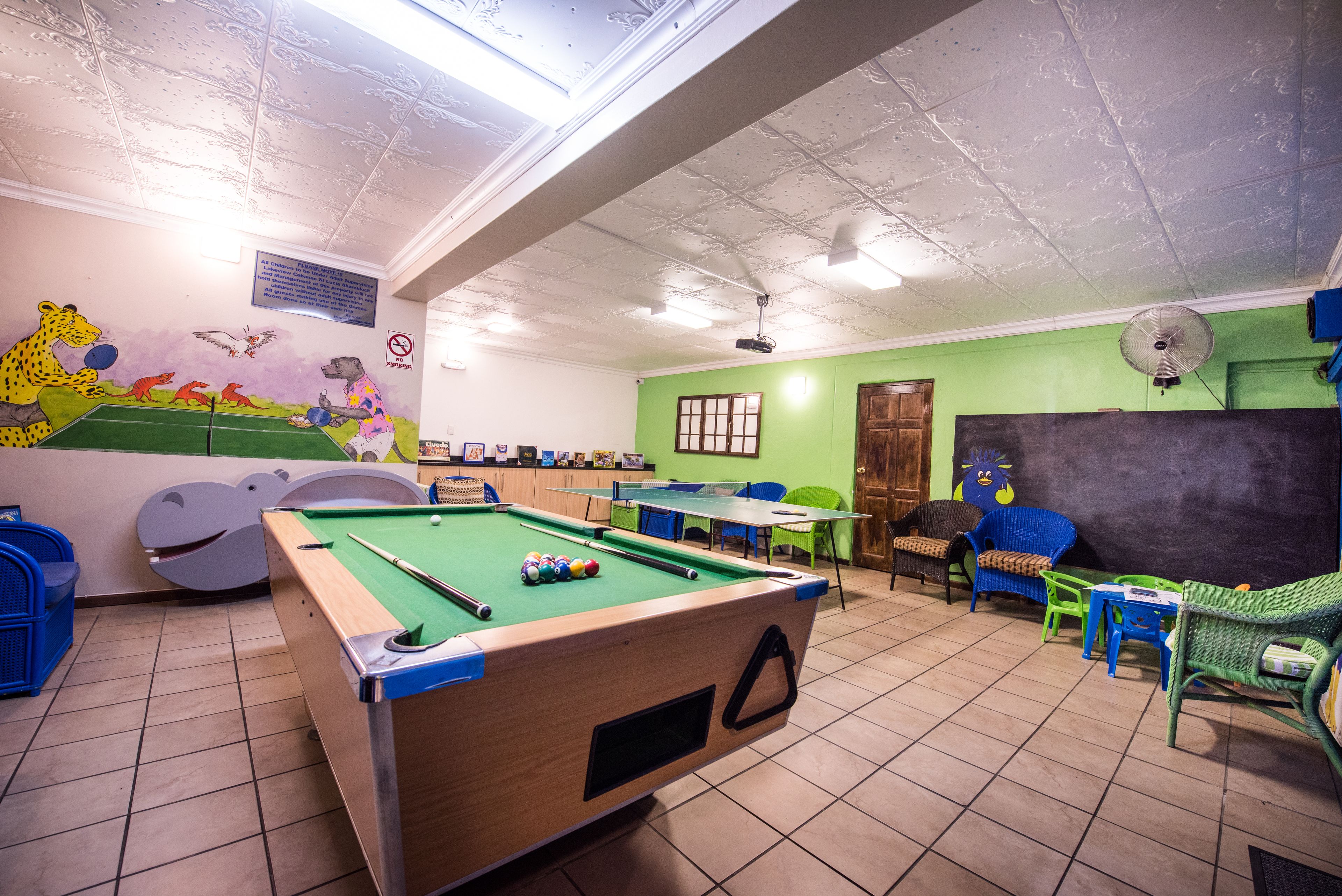 A pool table with balls, a ceiling fan, and a mural with animals on the wall.