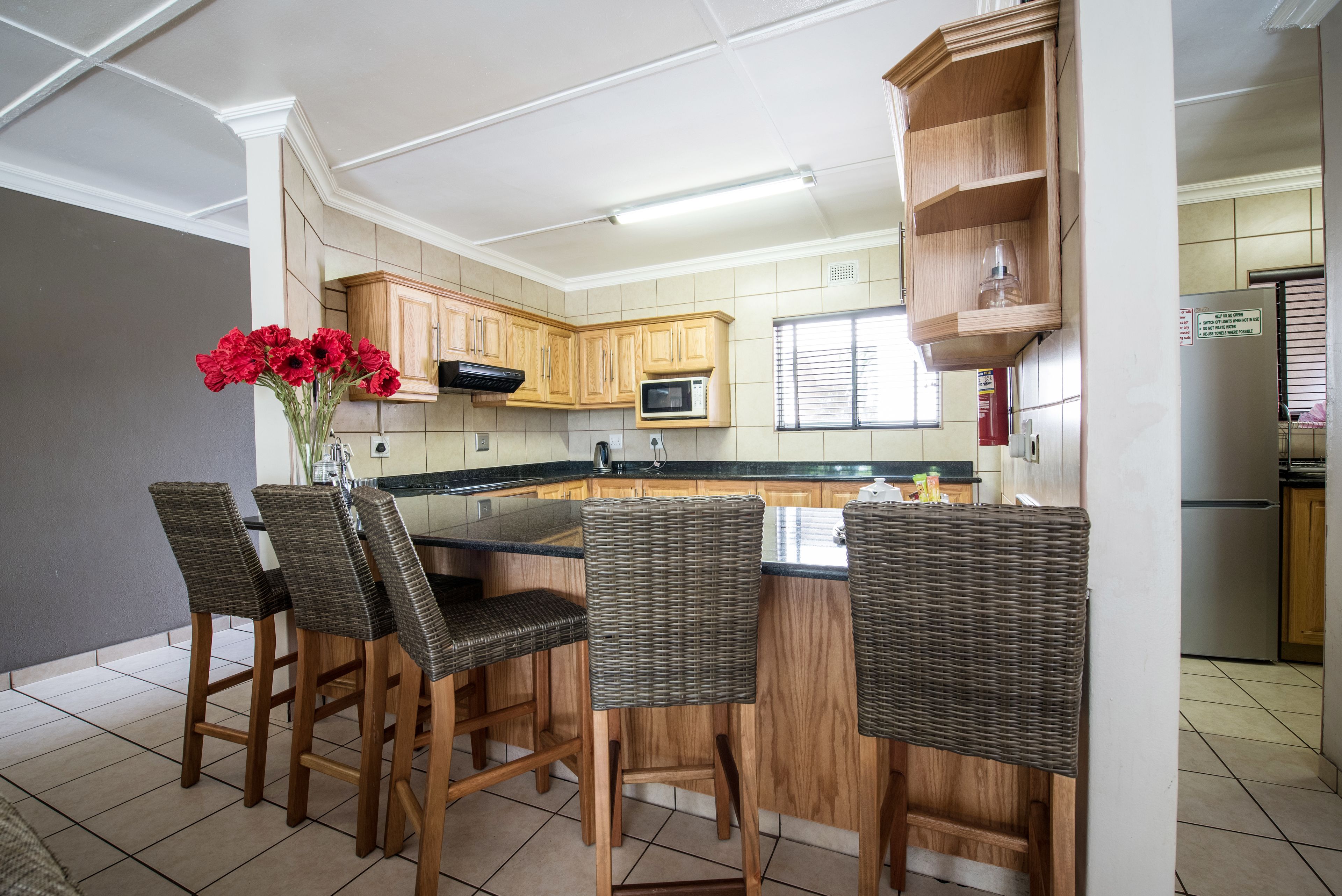 A kitchen with a central island, wooden cabinets, a microwave, and a refrigerator. There are four wicker chairs around the island.