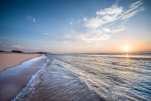 Una playa con cielo despejado y el sol poniéndose en el horizonte.