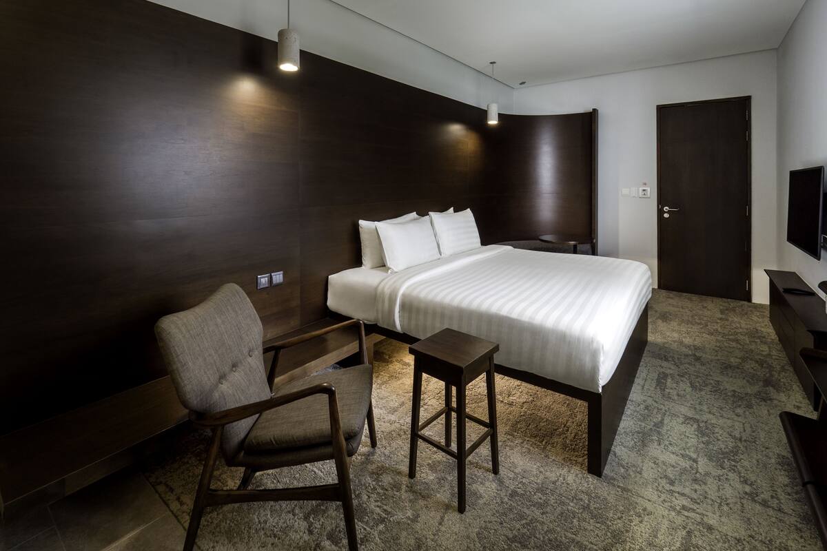 A modern hotel room with a large bed, a chair, a small table, and a TV.