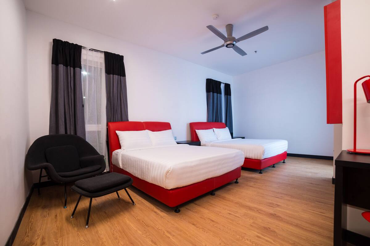 A hotel room with two beds, a chair, a desk, and a ceiling fan.
