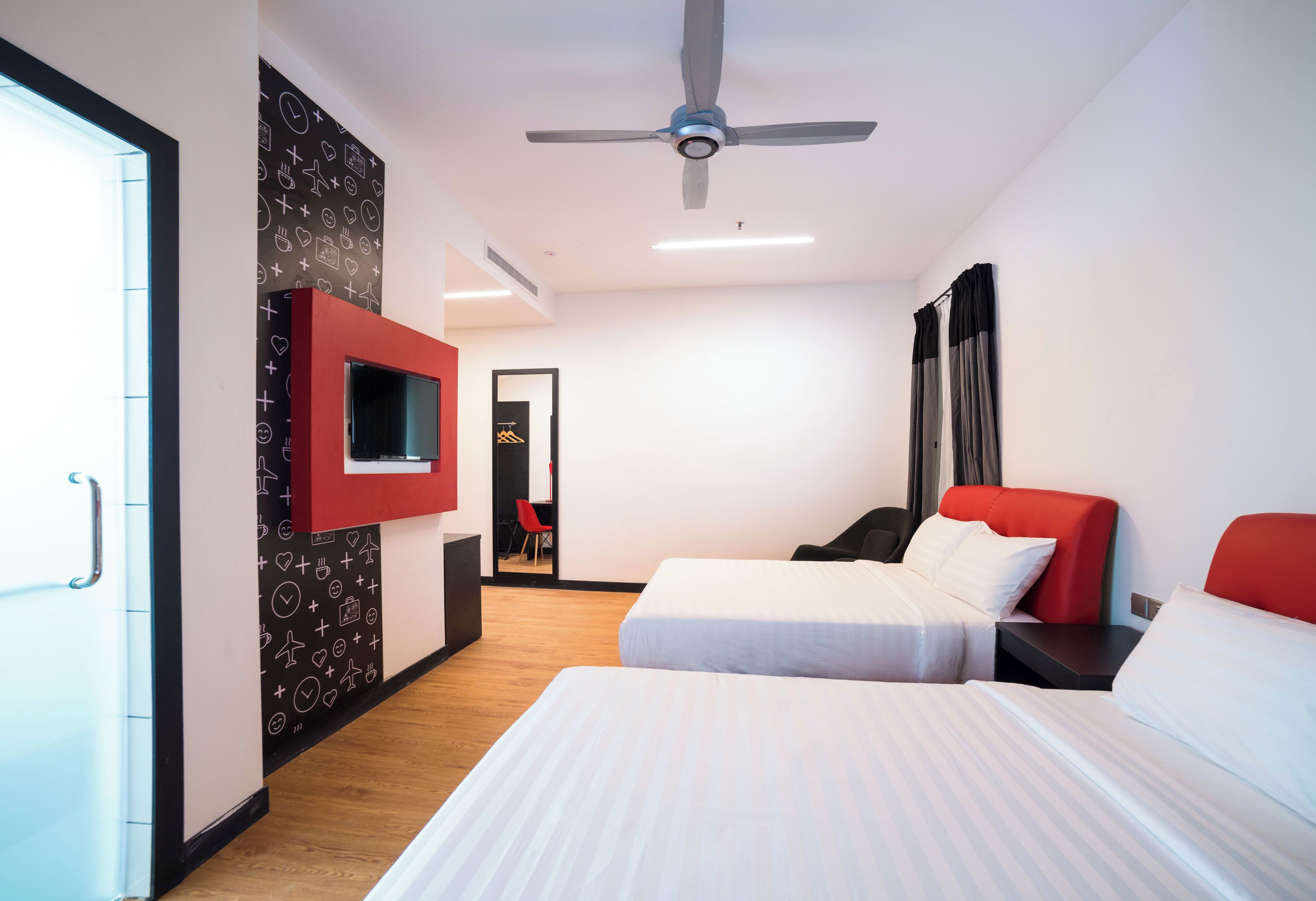 A modern hotel room with two beds, a TV mounted on the wall, and a ceiling fan.