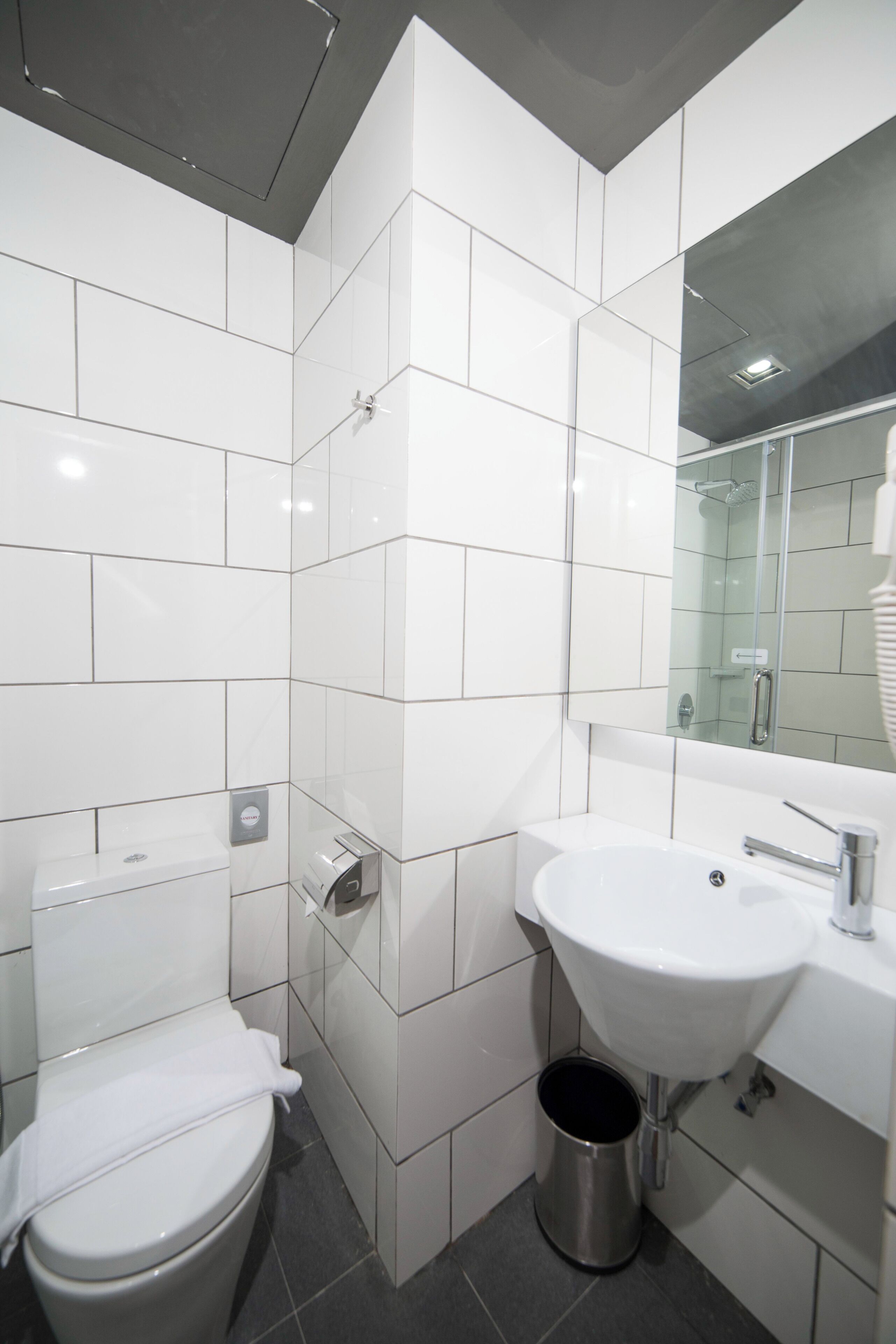 A modern bathroom with white tiles, a toilet, a sink, and a mirror.