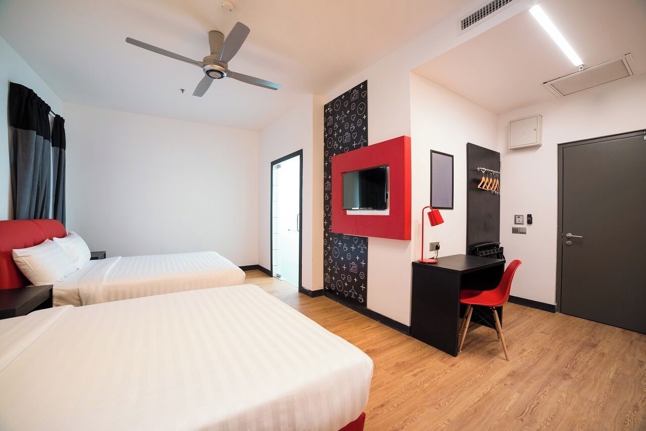 A hotel room with two beds, a desk with a chair, a TV, and a ceiling fan.