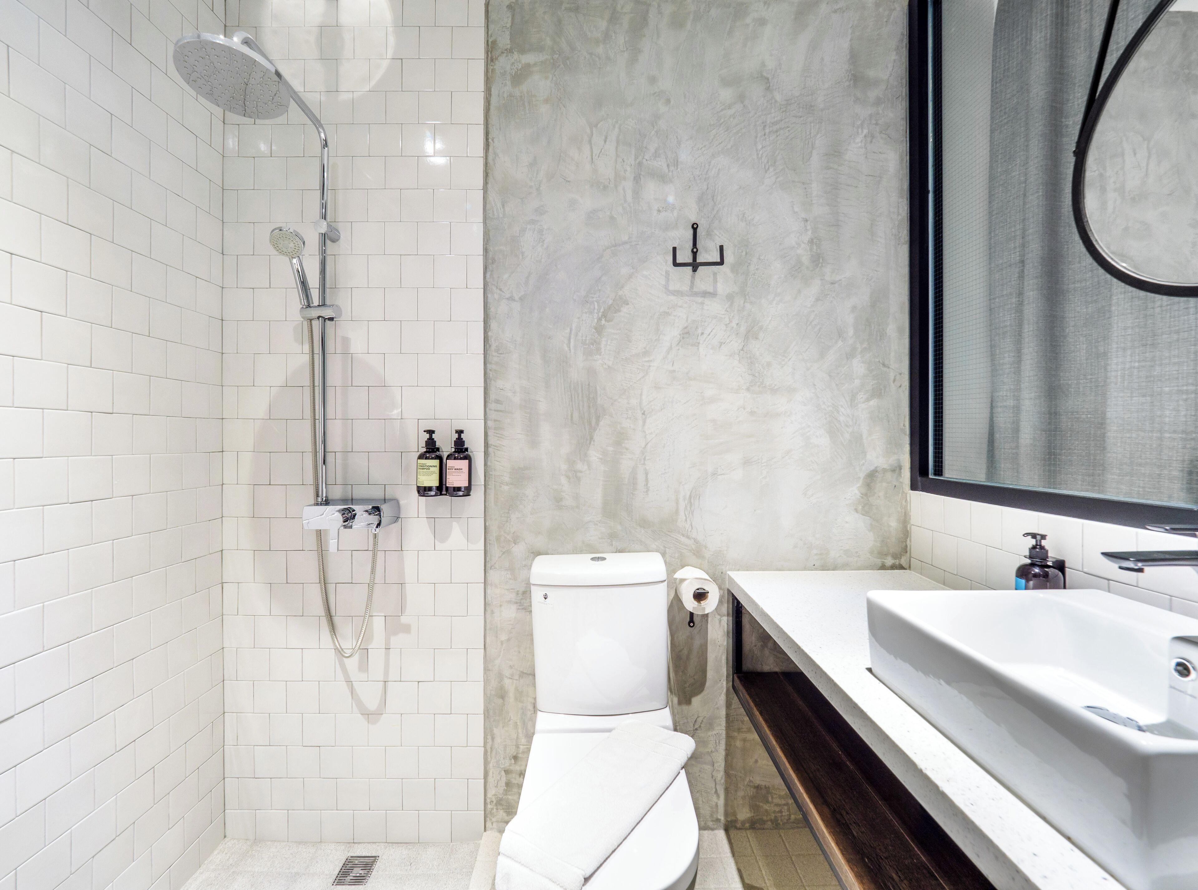 Un baño moderno con paredes de azulejos blancos, ducha, inodoro y lavamanos con espejo.