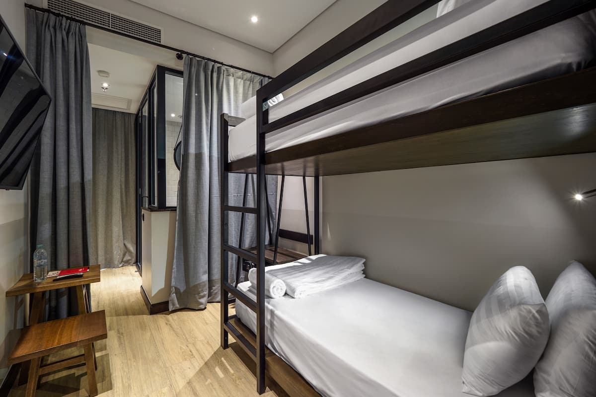 A bunk bed room with a wooden desk, a small table, and a window with curtains.