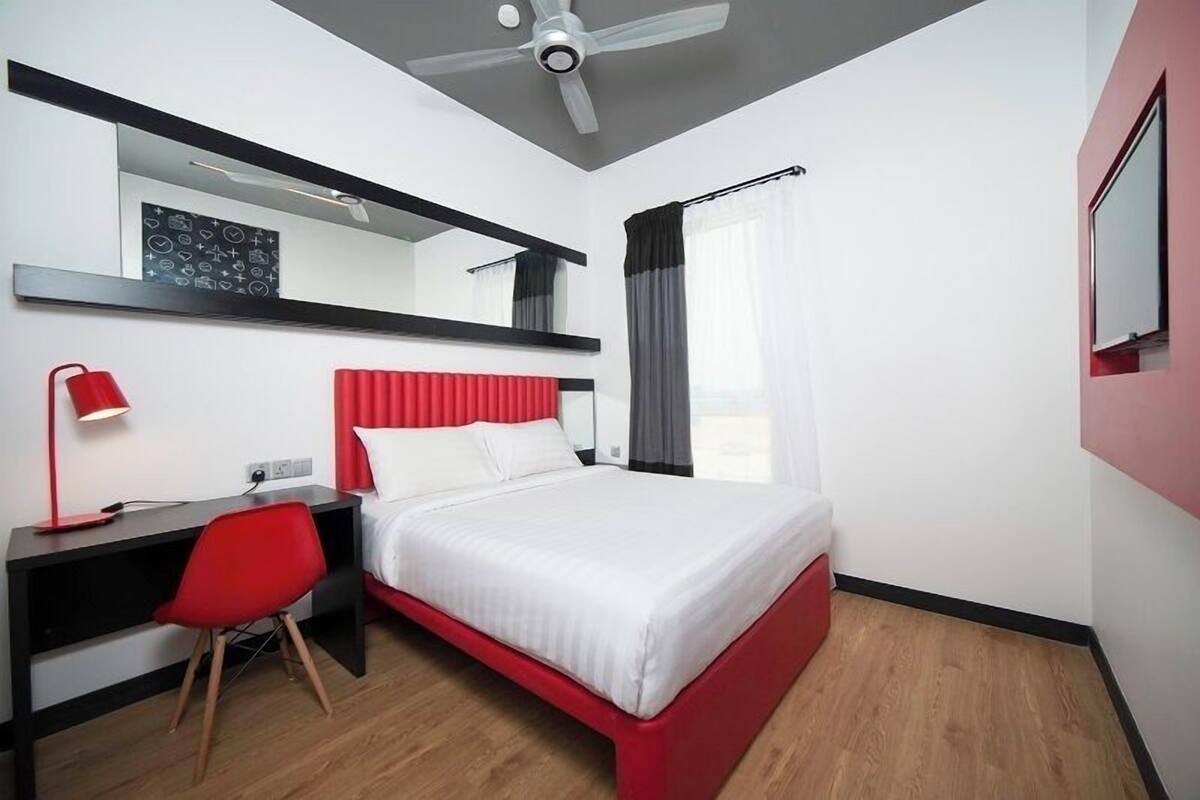 A hotel room with a bed, a desk, a chair, a ceiling fan, and a large mirror.
