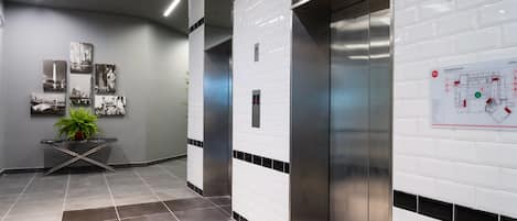 A modern elevator area with a tiled floor, a potted plant, and a wall-mounted emergency plan sign.