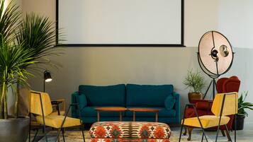 A living room with a teal sofa, two yellow chairs, a patterned ottoman, a floor lamp, and a large round mirror.