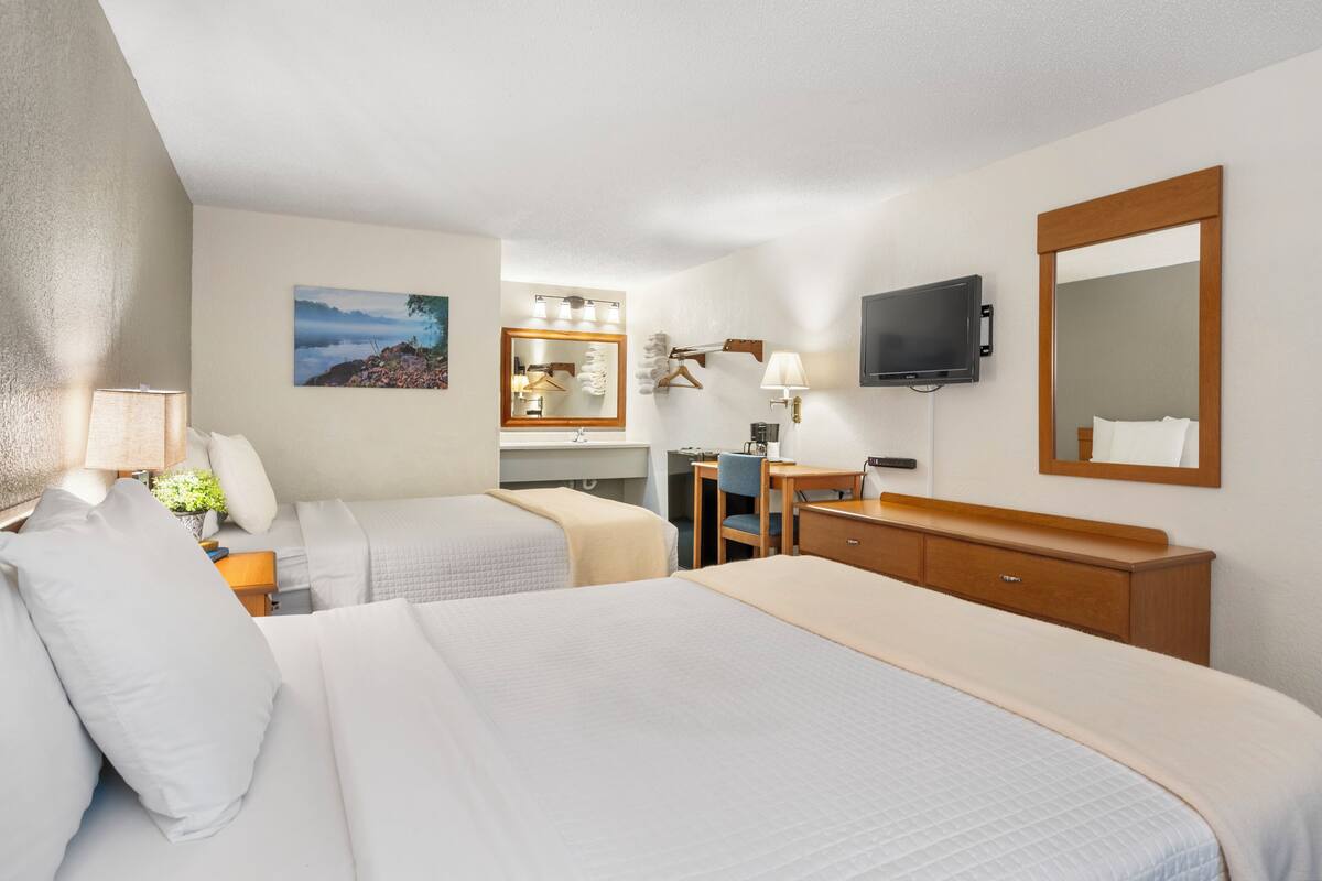 A hotel room with two beds, a desk, a chair, a TV, and a mirror.