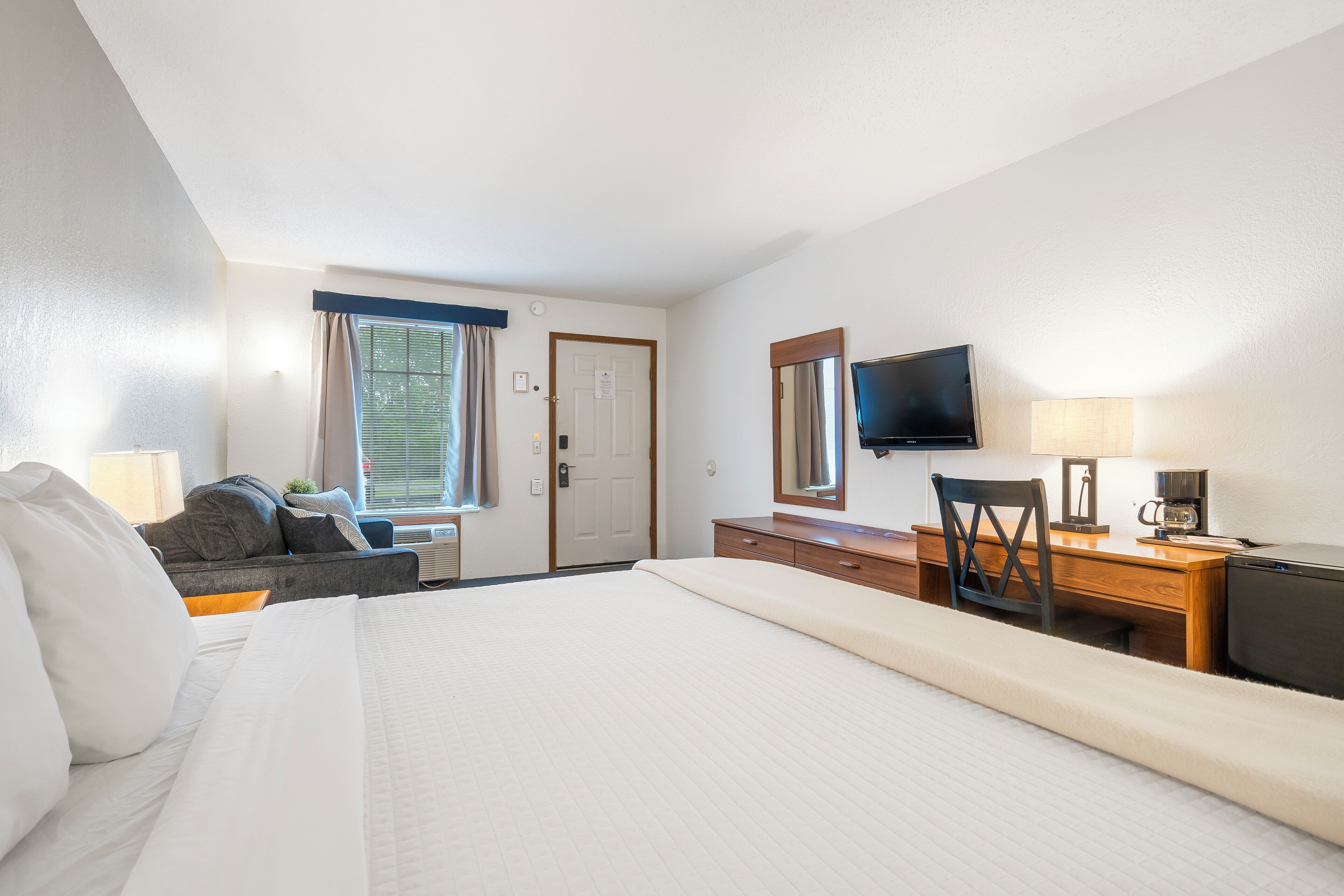 Ein Hotelzimmer mit einem großen Bett, einem Schreibtisch mit Stuhl, einem Fernseher und einem Fenster mit Vorhängen.