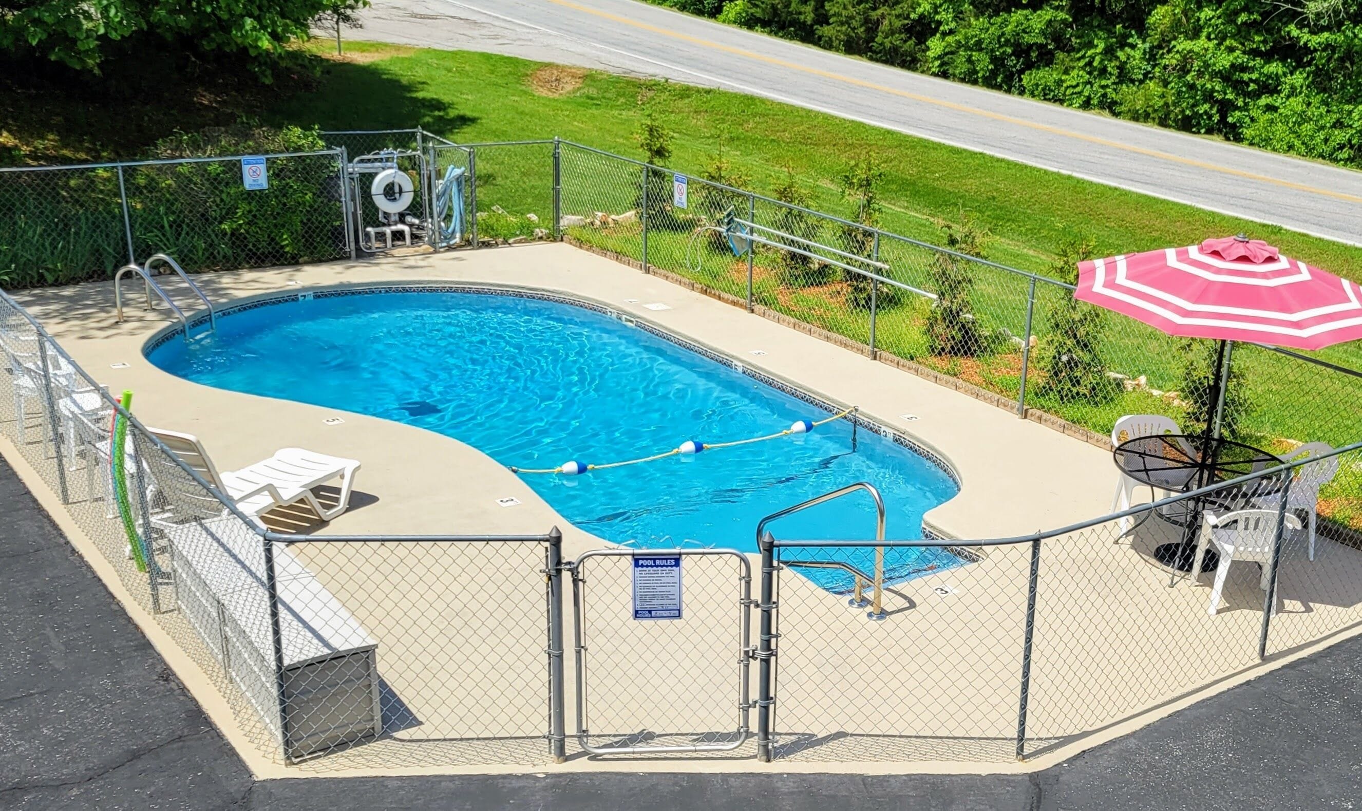 Una piscina rectangular con un deck cercado, una escalera de piscina y un cartel con las normas de la piscina.