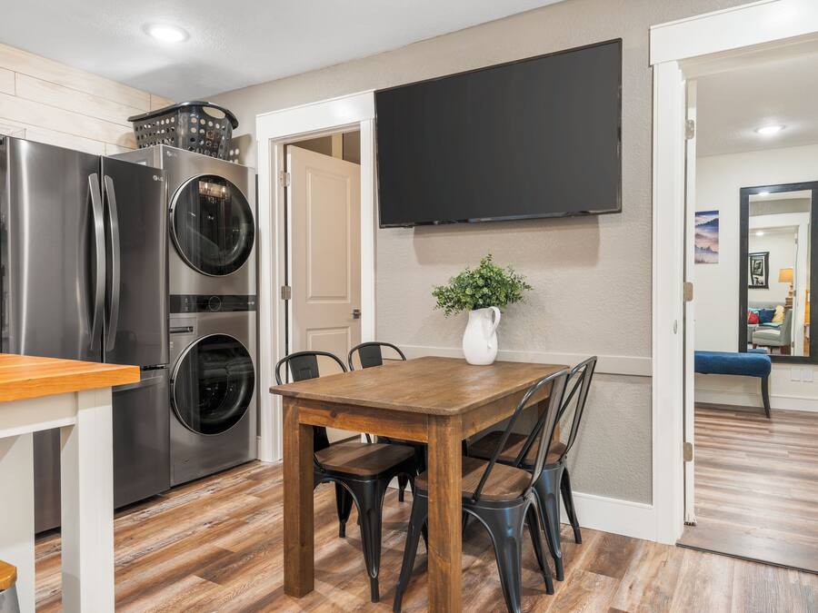 A modern kitchen with stainless steel appliances, a wooden dining table, and a flat-screen TV mounted on the wall.