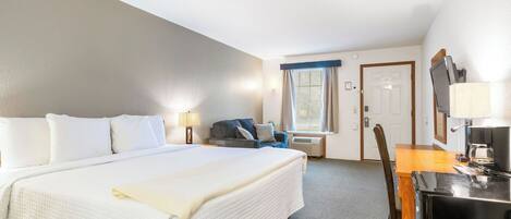 Habitación de hotel con una cama grande, un escritorio con ordenador, una silla, una ventana con cortinas y una puerta.