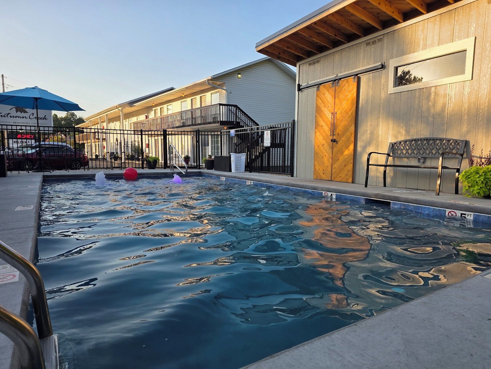 A swimming pool with a wooden deck, a bench, and a building with a large door.