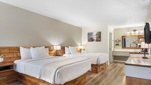 A hotel room with two beds, a wooden headboard, bedside lamps, a small plant, and a bathroom with a mirror and sink. - Autumn Creek Branson (Branson)