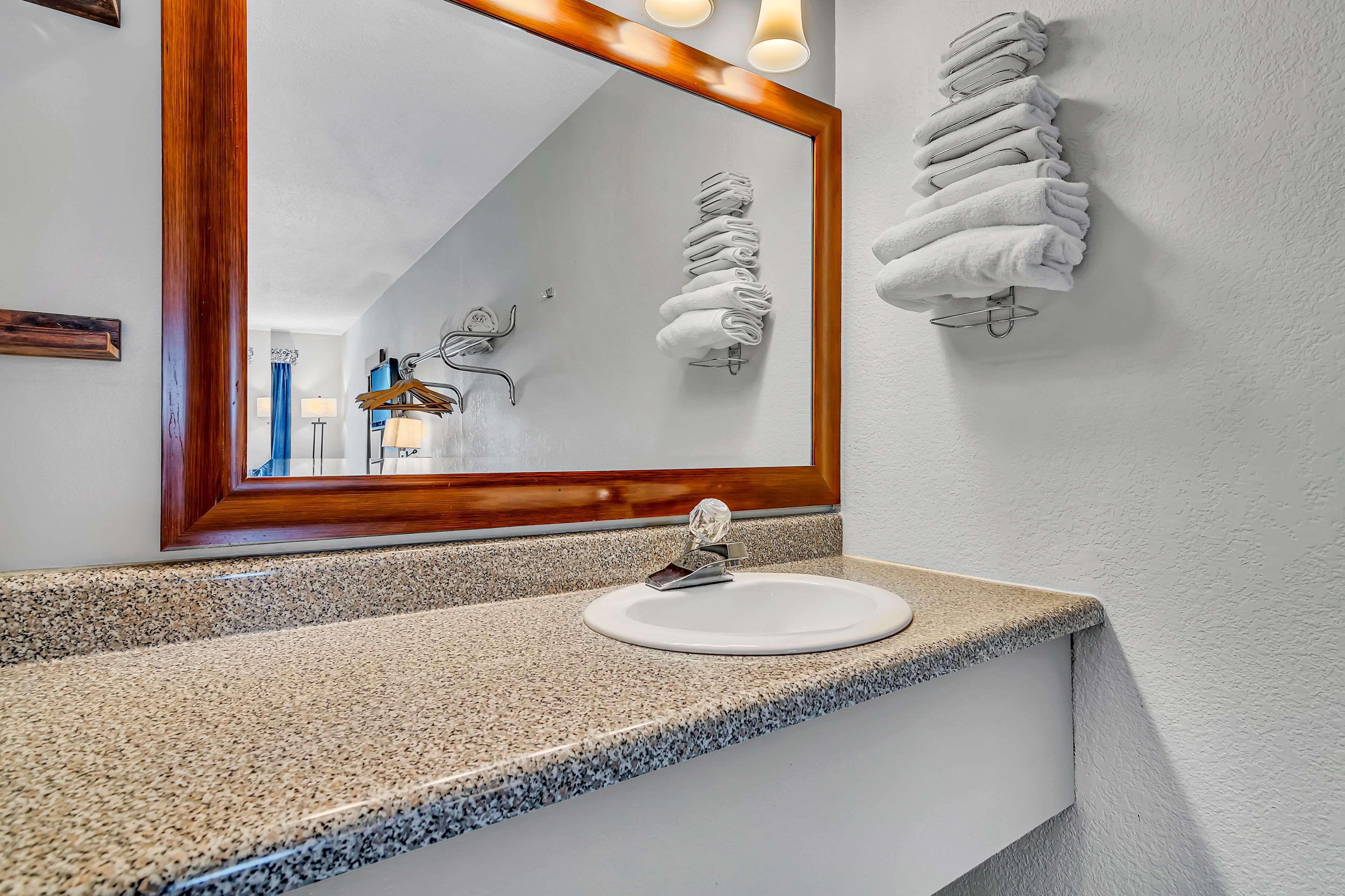 A bathroom with a granite countertop, a white sink, and a mirror with a wooden frame.