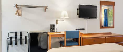 Una camera d'albergo con un letto, una scrivania con lampada, una televisione, uno specchio, una sedia, un piccolo frigorifero e un portasciugamani.