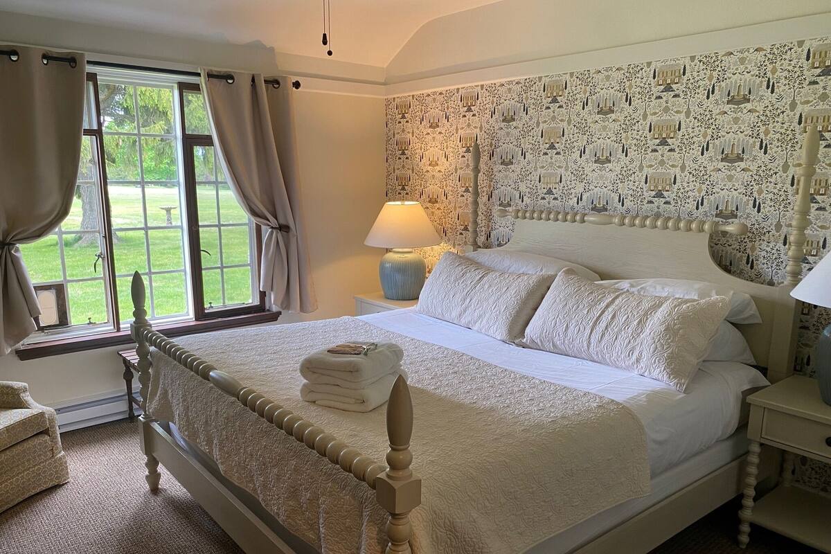 A neatly made bed with a headboard, a bedside lamp, and a window with curtains.