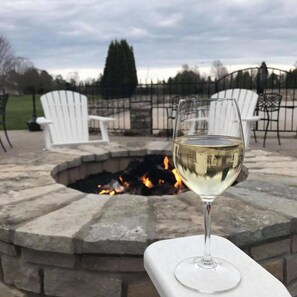 A glass of white wine on a white table with a stone fire pit in the background. - Maxwelton Braes Lodge and Golf Course (Baileys Harbor)