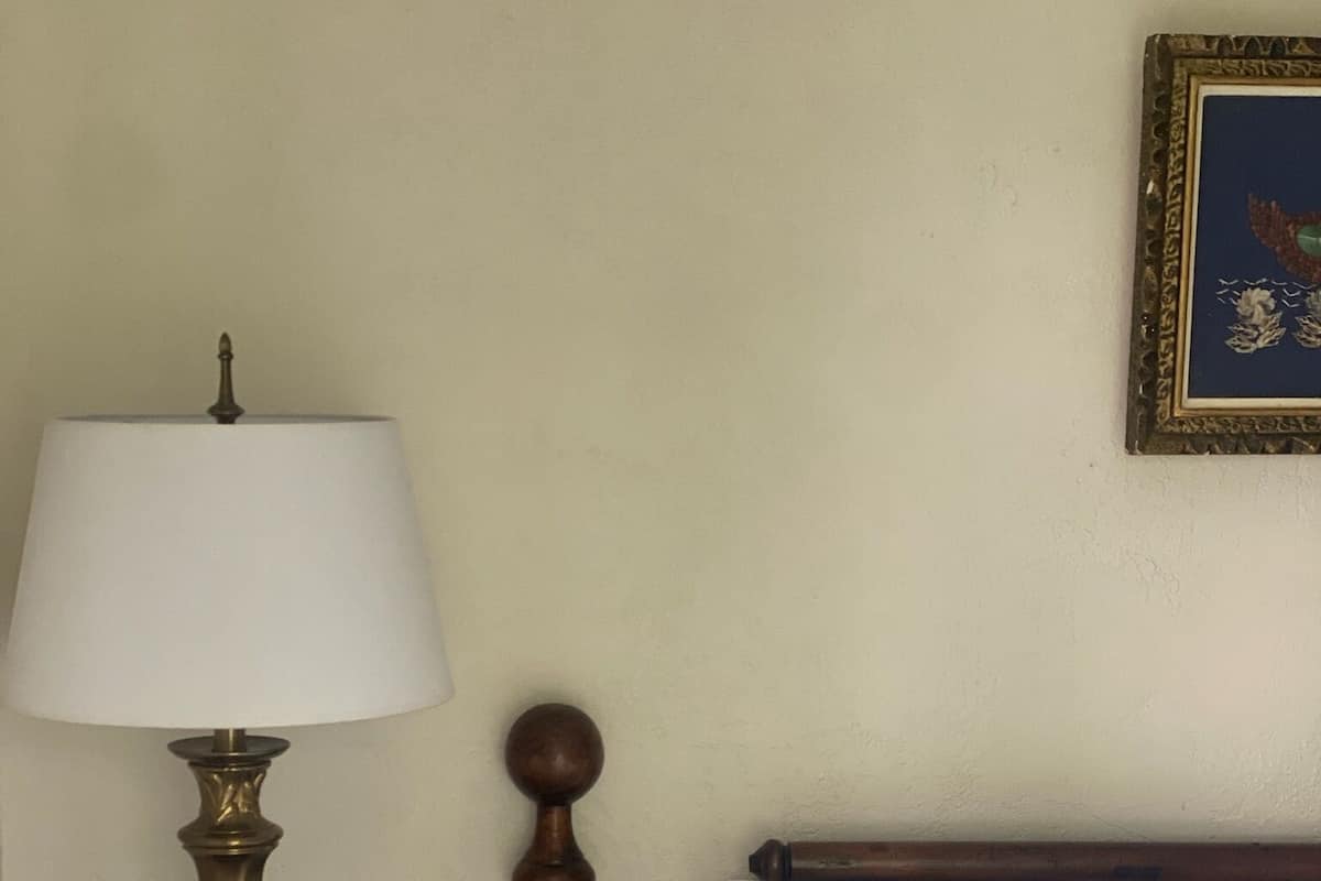 A bed with white bedding, a wooden headboard, and a nightstand with a lamp.