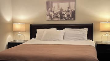 A hotel room with a large bed, two bedside tables with lamps, a framed picture on the wall, and a brown headboard.