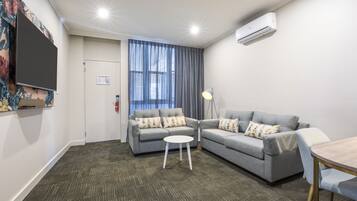 Una sala de estar moderna con dos sofás grises, una mesita blanca y un televisor montado en la pared.