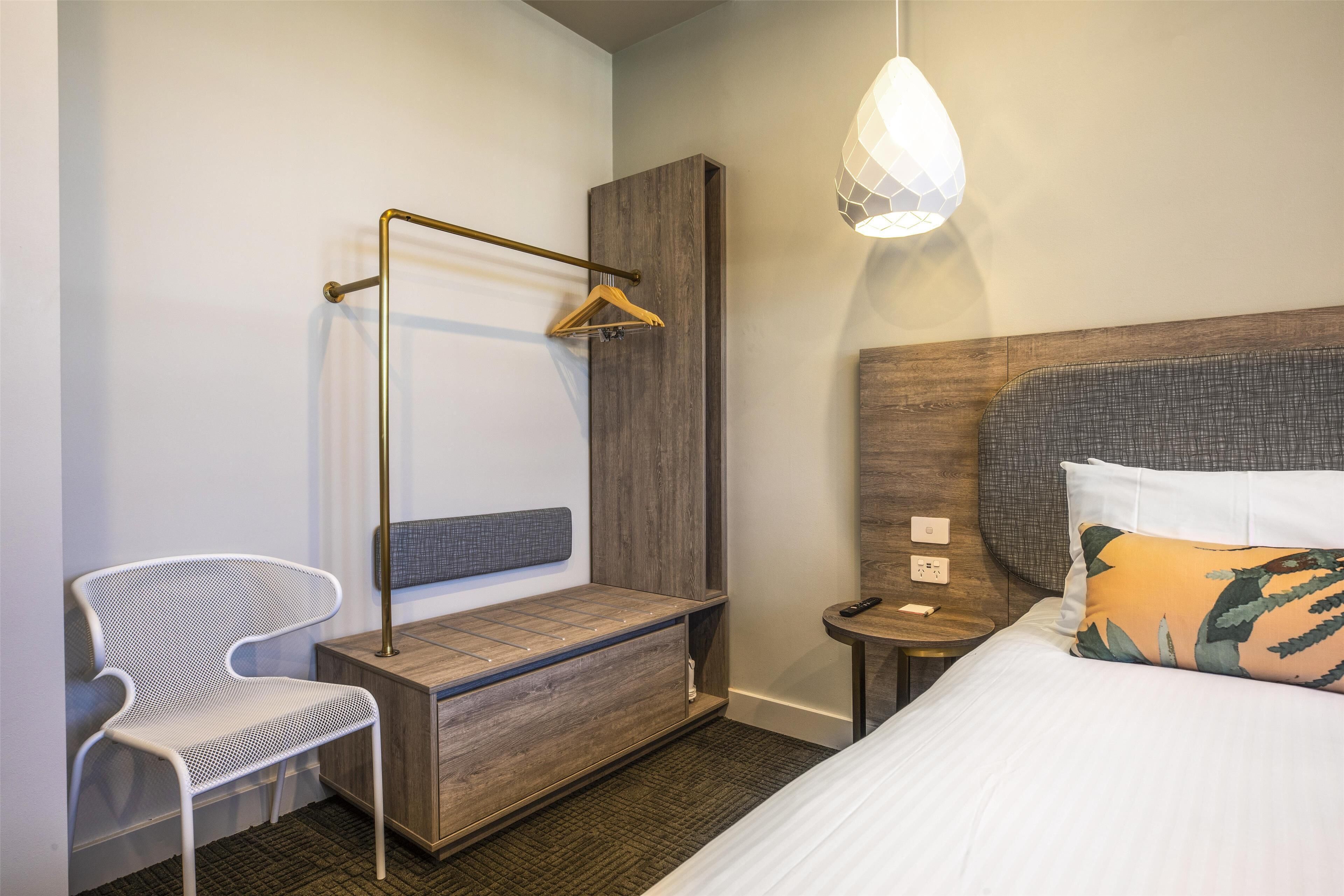 Et moderne hotelværelse med seng, hængende brusebad, stol og natbord med lampe.