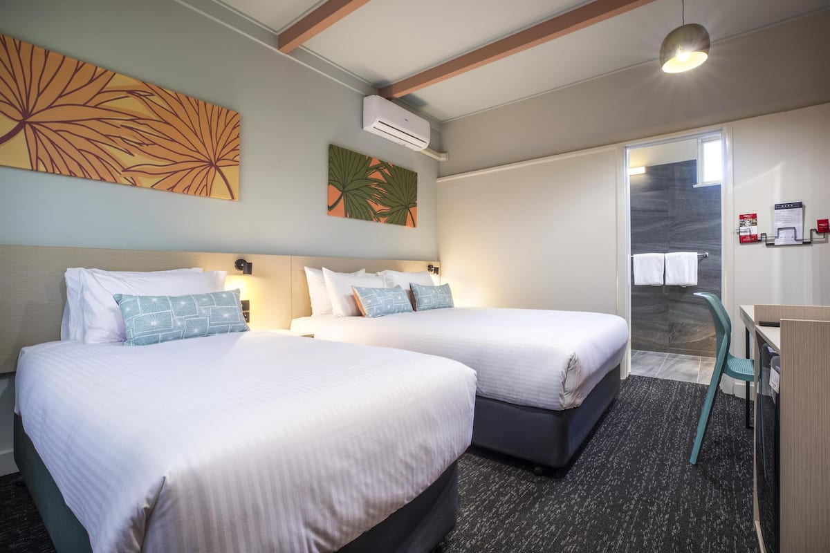 A hotel room with two beds, a desk, and a shower area.